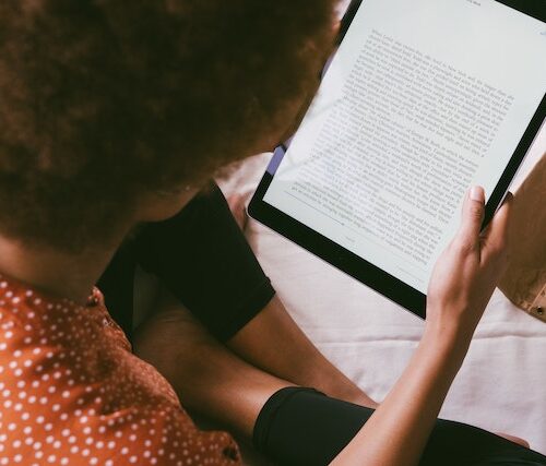 Girl with pretty afro and red polka dot shirt reading kindle.