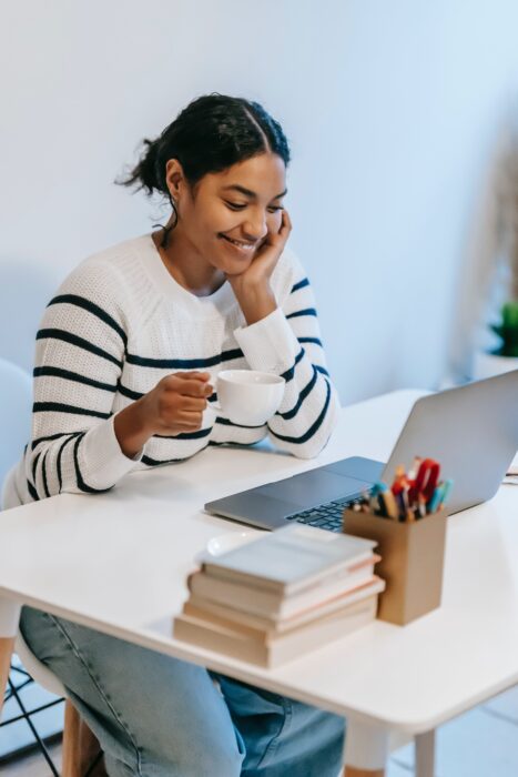 Young woman browsing the internet for books with a stack of books beside her.