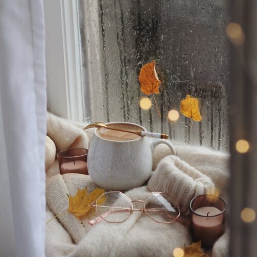 Cozy mug by the window with fall decorations, including leaves and pumpkins, creating a warm and inviting autumn atmosphere.