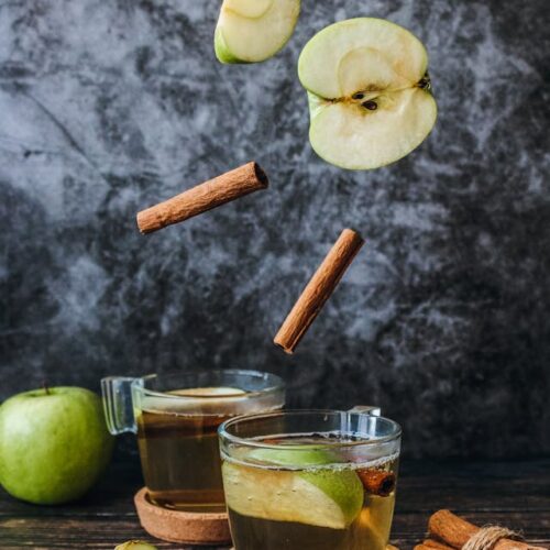 Steaming mug of cannabis-infused hot apple cider with cinnamon sticks and apple slices